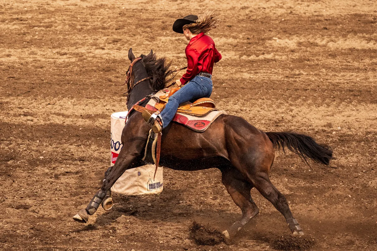 A rider in a red shirt leaning a brown horse around a barrel at a rodeo in Washington state.